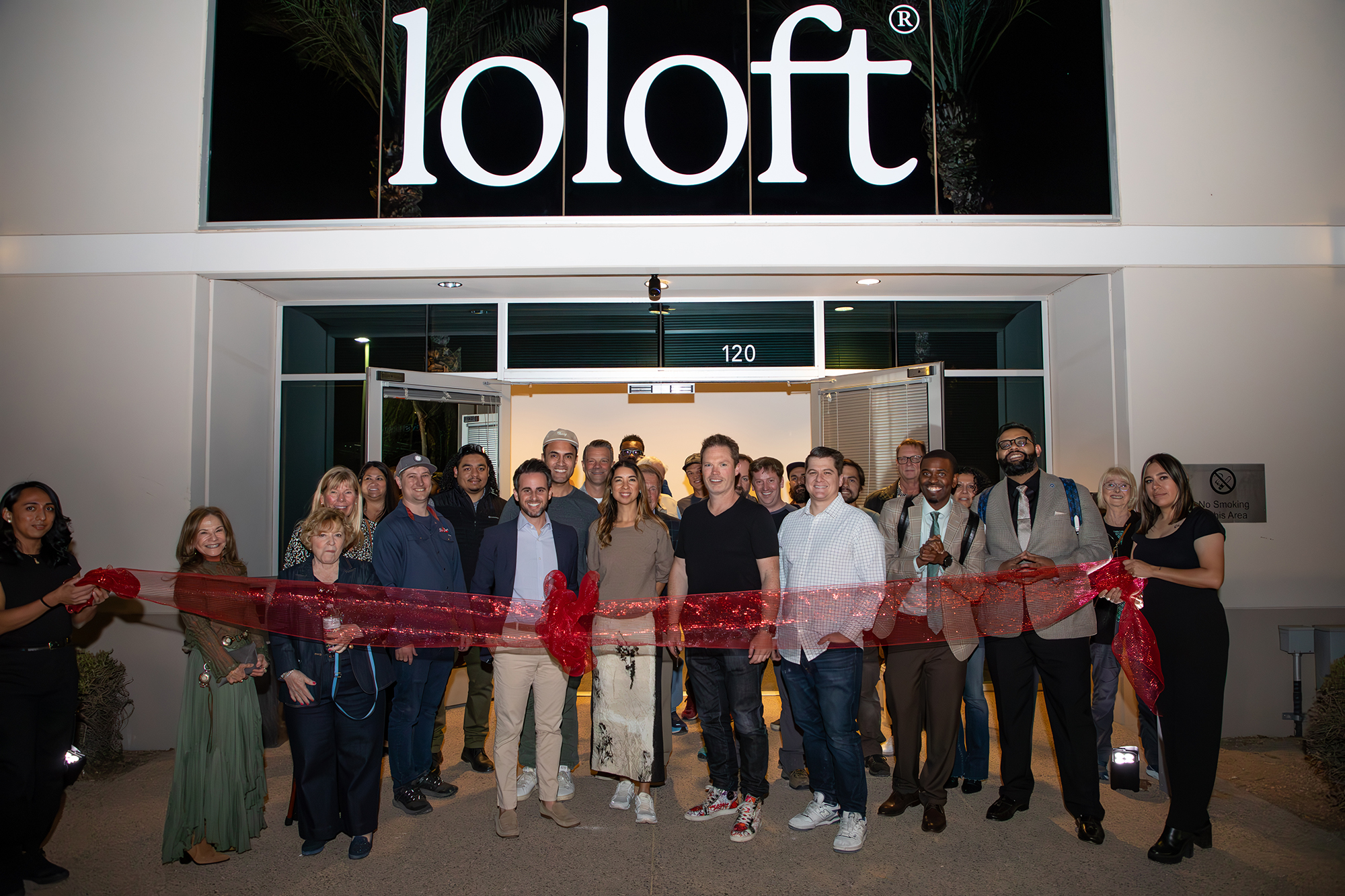 A group of people stand behind a red ribbon, under the large Loloft nameplate.