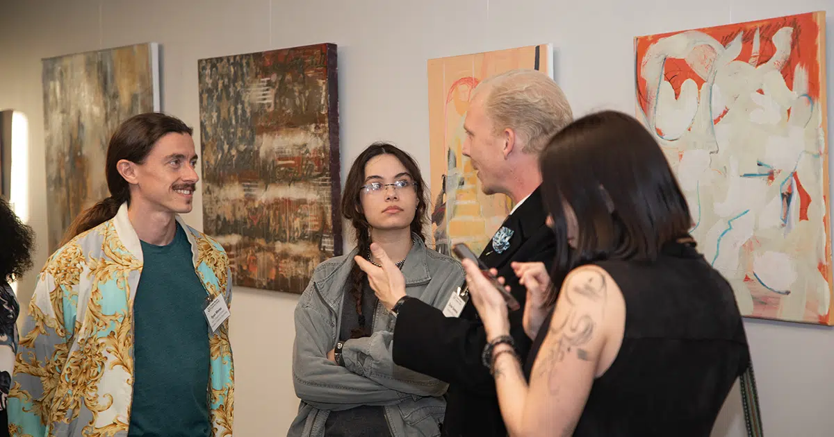 Two men and two women stand in front of large art pieces on the wall behind them, speaking to each other.