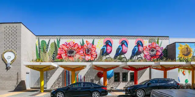 A mural on a gray building shows colorful flowers and birds.