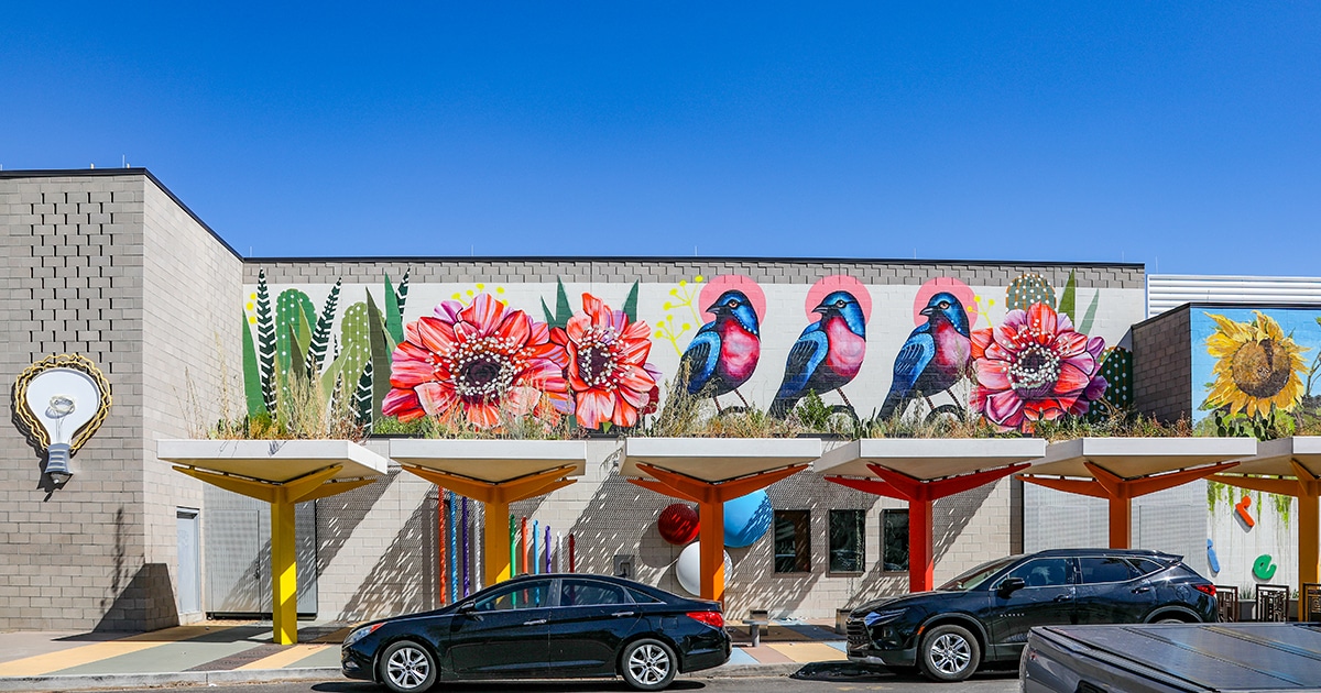 A mural on a gray building shows colorful flowers and birds.