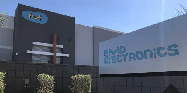 The EMD building with a light blue logo in the background, and a sign with the company's full logo in the foreground.