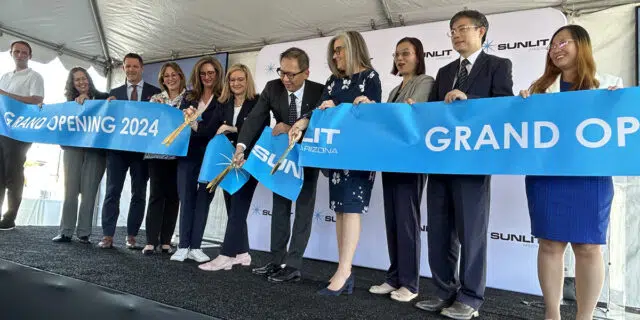 A line of men and women dressed in professional clothing cut a blue ribbon that announces Sunlit's grand opening.