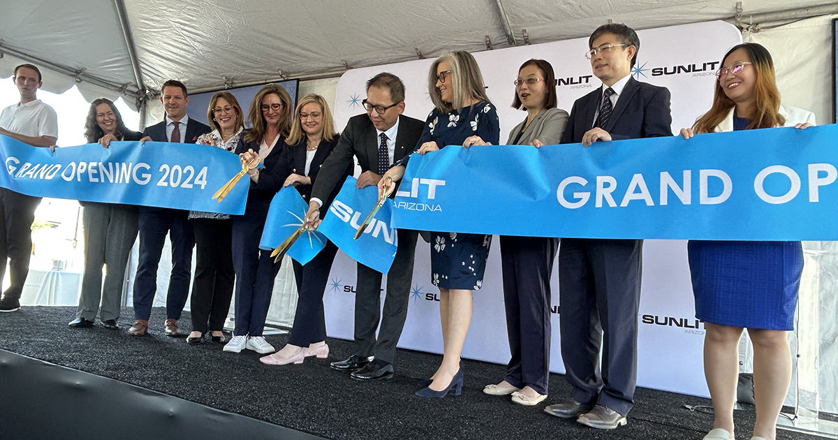 A line of men and women dressed in professional clothing cut a blue ribbon that announces Sunlit's grand opening.