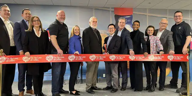 A line of people stand with a pair of giant red scissors behind a red ribbon at a Nestle facility.