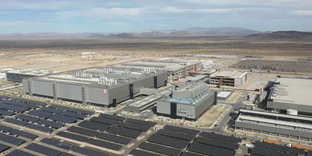 Five buildings of TSMC's massive facility stand together behind rows of solar panels.