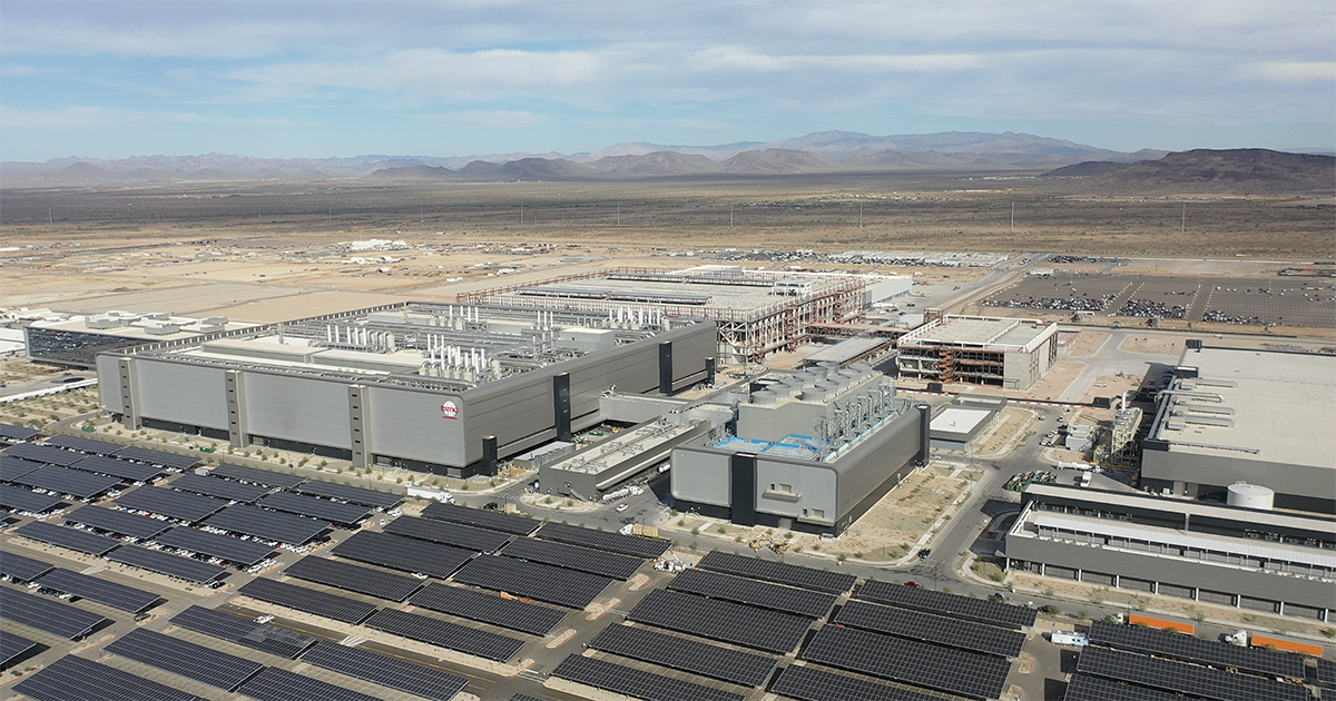 Five buildings of TSMC's massive facility stand together behind rows of solar panels.