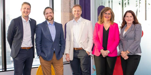 A line of three men and two women in professional clothing pose for a picture.