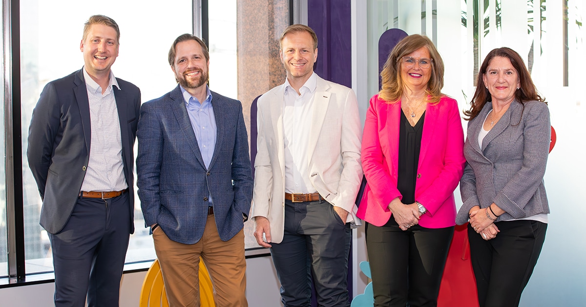 A line of three men and two women in professional clothing pose for a picture.